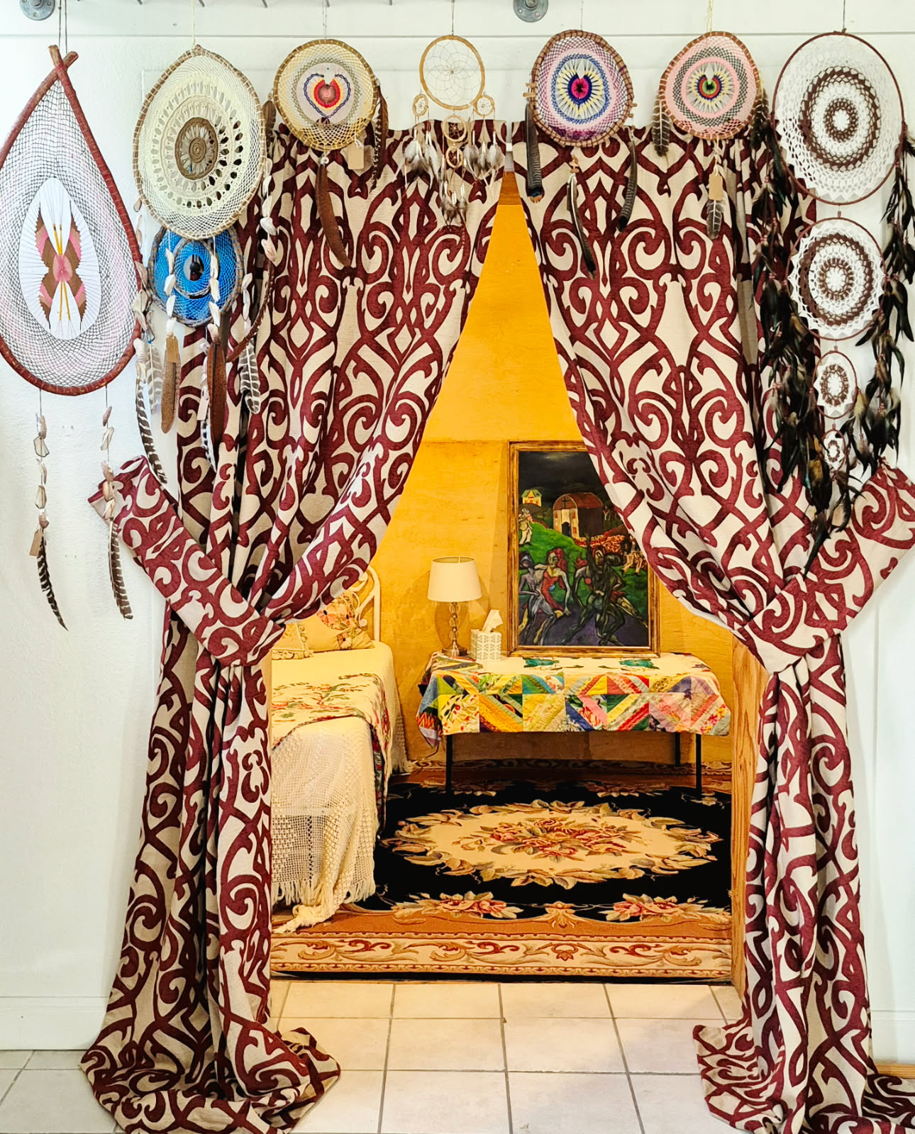 A curtained corner with a patterned rug, a small table and a framed painting