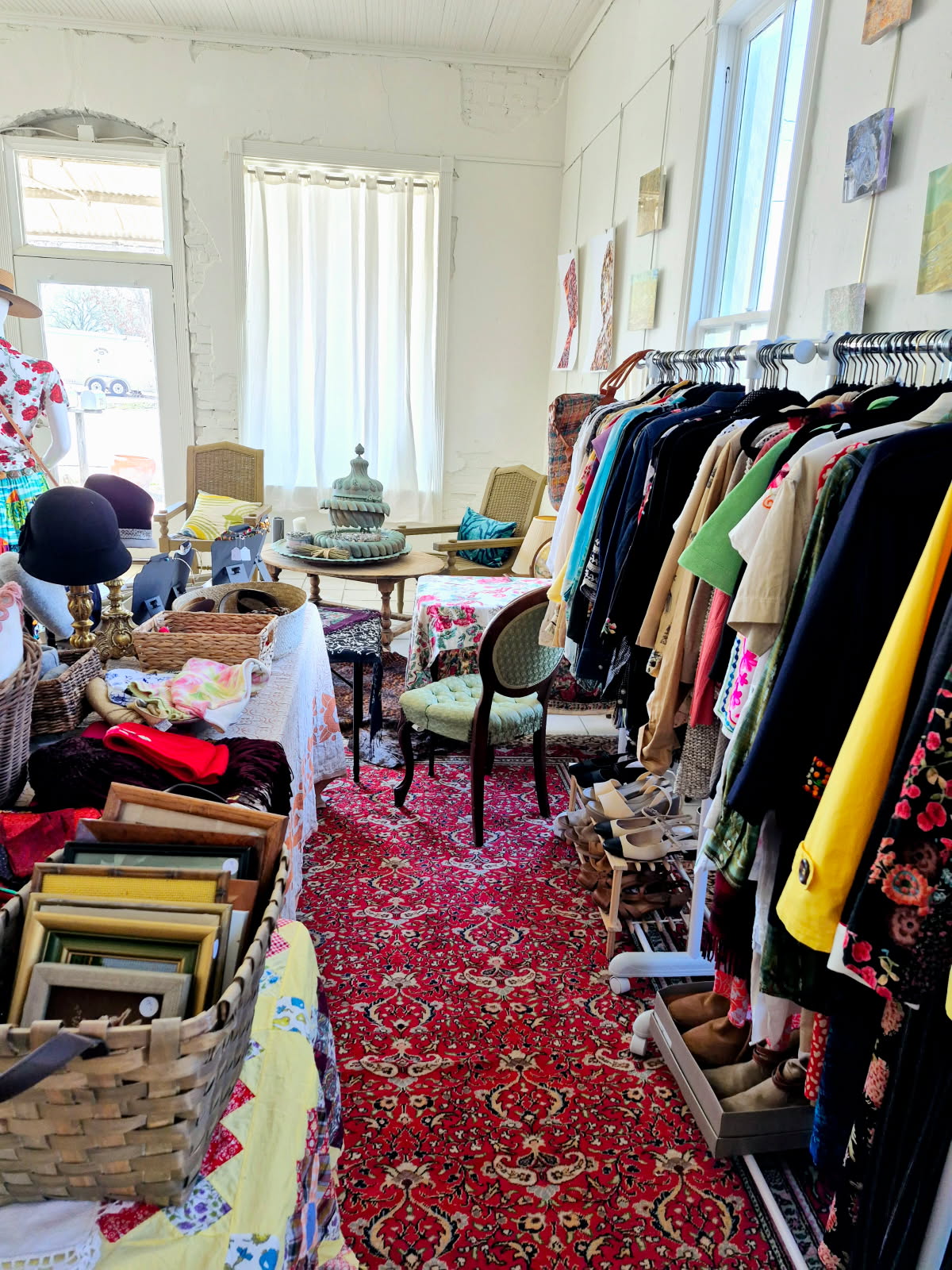 The shop floor, with racks of clothing around a table of glassware and stacked frames