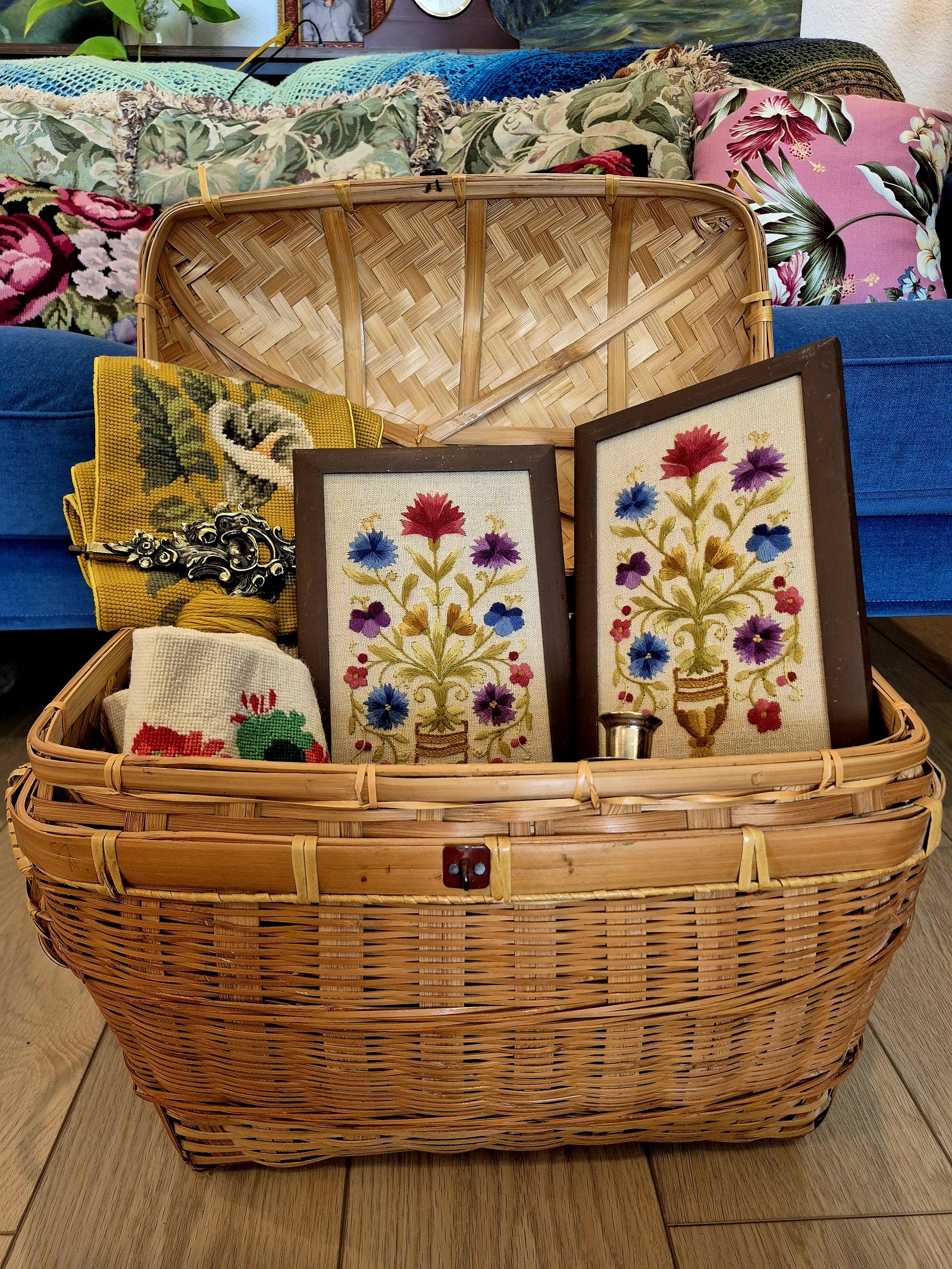 A woven basket filled with framed floral embroidery and textile work